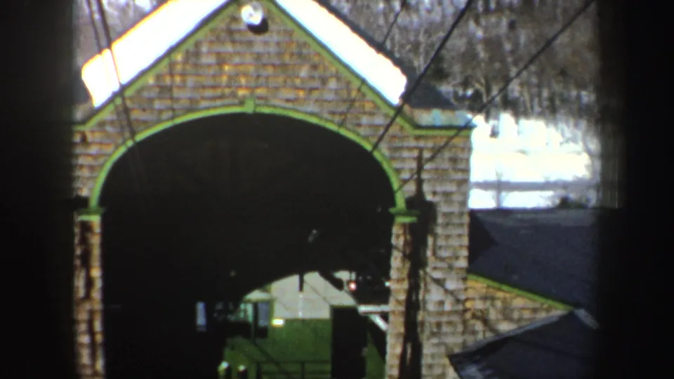 1962 New York home-movie frame of a green-trimmed brick arch and shadowed entrance, with winter snow visible nearby.