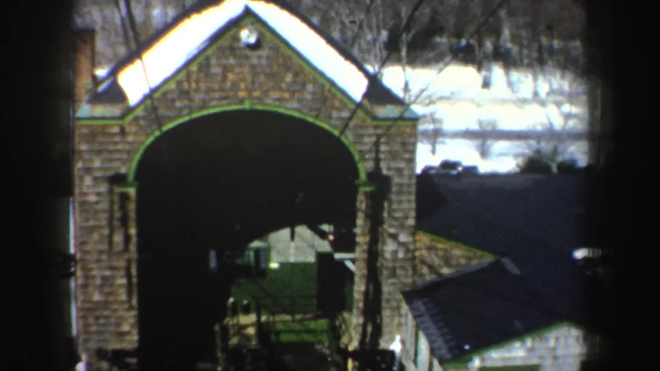 1962 New York 8mm view of a brick arched entrance with snow on roof edges, bare trees, and a small adjacent roofline.
