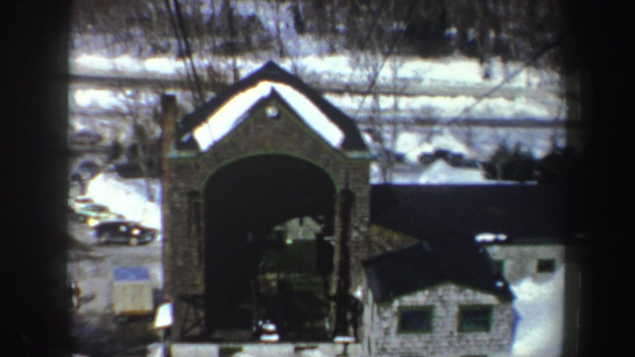 1962 New York home-movie frame from a ski lift, looking toward a stone-faced arched structure and snowy resort grounds.
