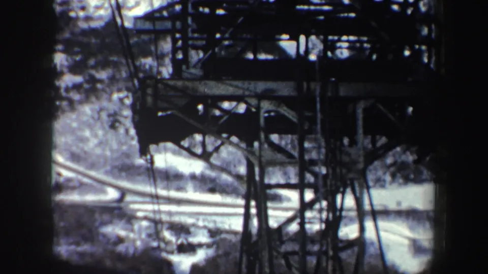 1962 New York 8mm lift-rider view showing metal support beams, cables, snowy ground, and a curving road or path.