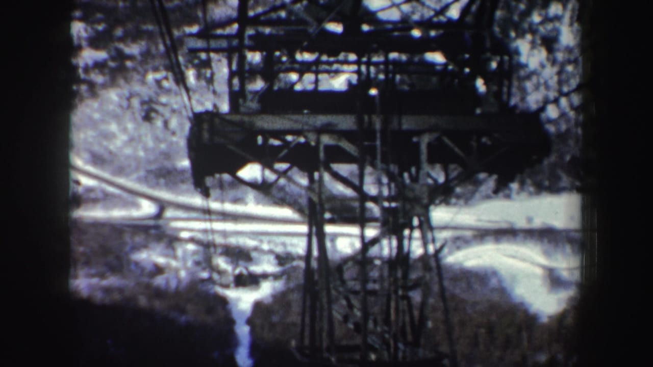 Steel tram tower and cables above snowy wooded mountains, with dark film borders.