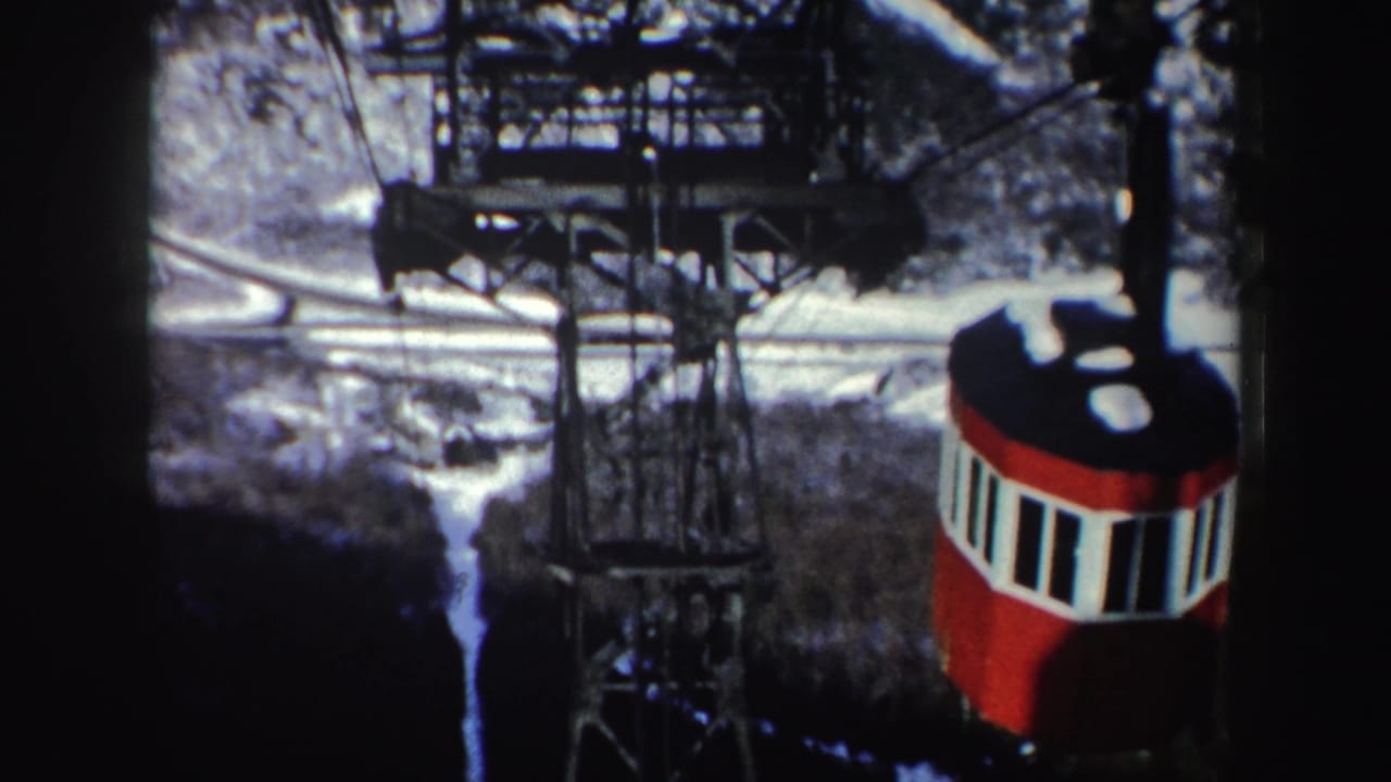 Red and white tram cabin beside cables and metal towers over snowy hills.