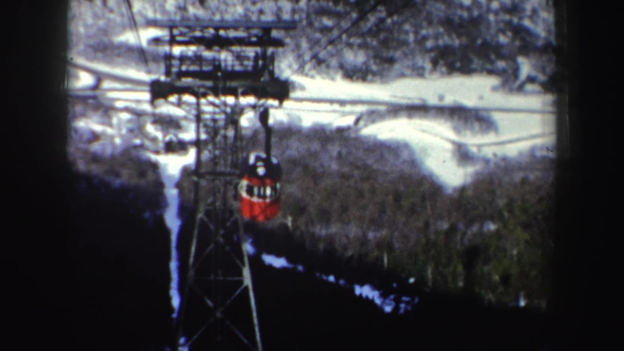 Red cable car descending beside a metal tower over snowy wooded terrain.
