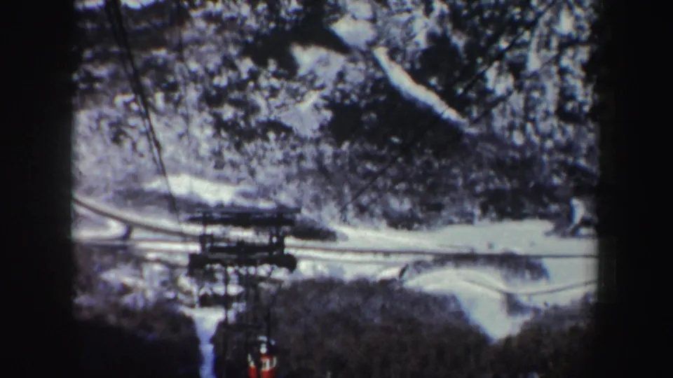 1962 New York 8mm frame showing the skyride tower and red cable car amid snow, trees, and mountain road shapes.