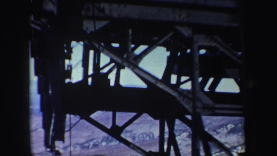 1962 New York home-movie frame with cable-car girders and cables silhouetted against distant winter terrain.