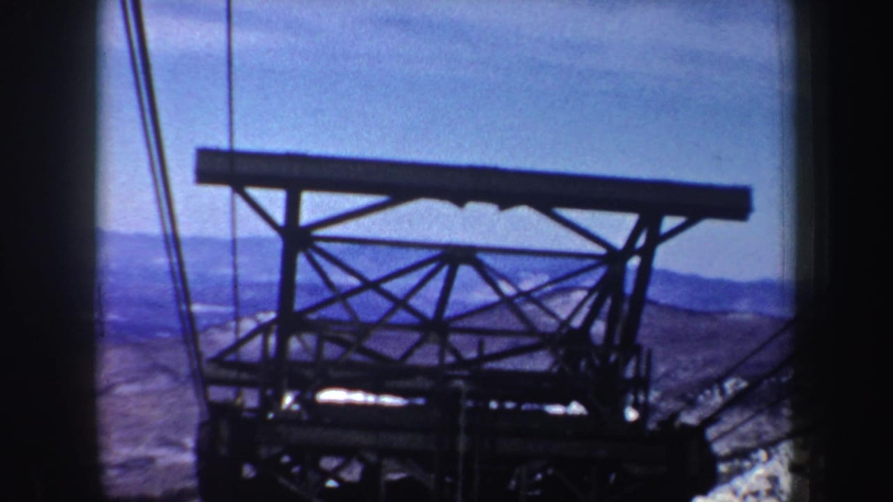 Steel cableway tower and overhead cables against blue mountain ridges.