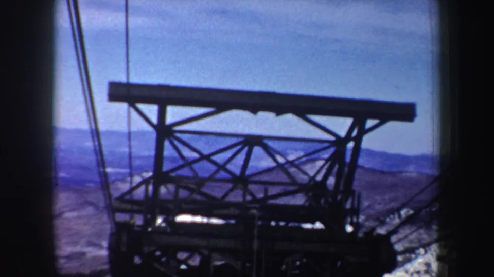 1962 New York 8mm frame showing a steel cableway tower seen from a passenger perspective with distant mountain ridges beyond.