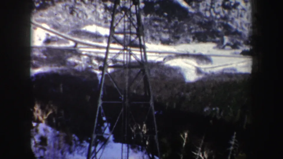 1962 New York 8mm frame showing a cableway support, dark foreground edge, and snowy wooded mountain terrain below.