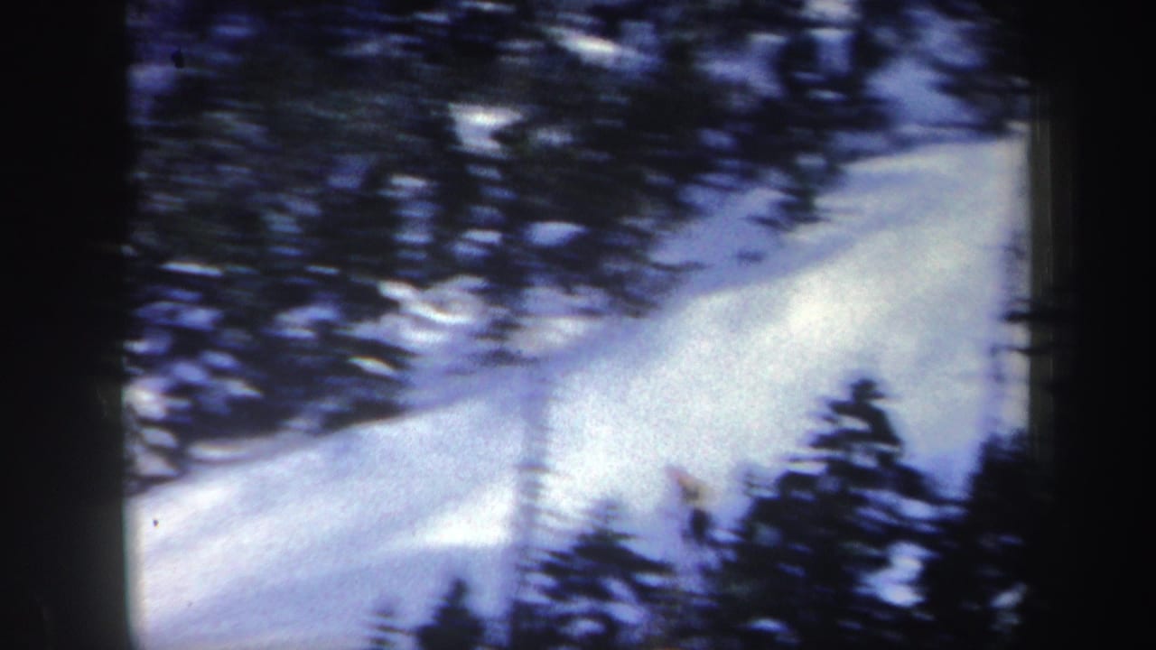 Distant skier on a snowy wooded slope seen through dark 8mm frame edges.