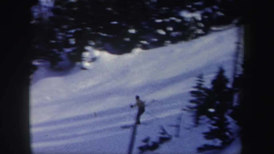 Distant 1962 New York ski footage frame with a lone skier on an open snowy bank beside winter trees.