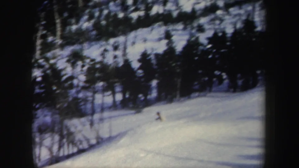 A distant skier crosses a snowy New York slope in 1962, with evergreens and winter shadows around the run.