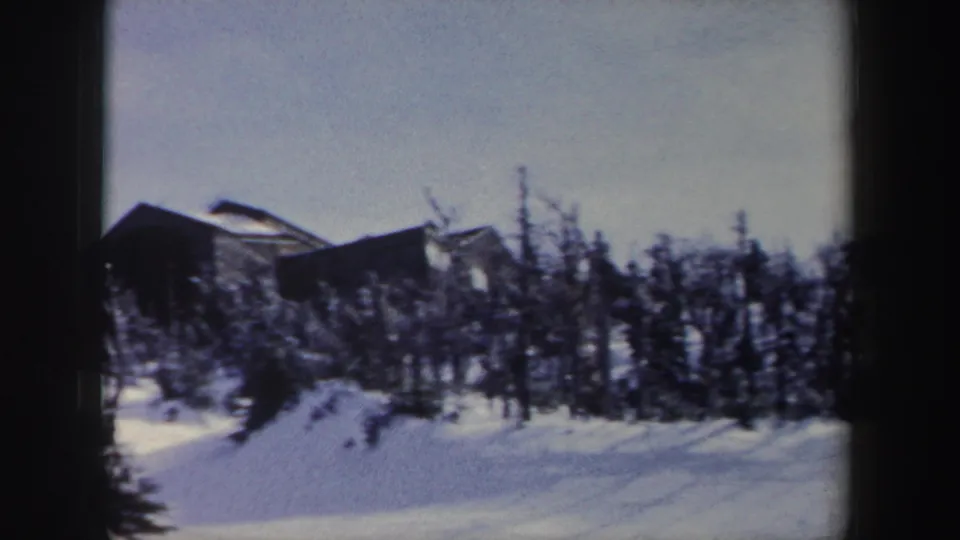 1962 New York 8mm frame showing a snow-covered clearing, leafless trees, and a distant dark building beyond the winter brush.