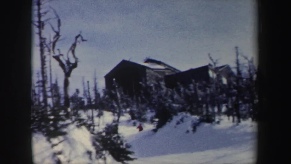 1962 New York 8mm frame with a distant non-identifiable building, bare trees, snowbanks, and a small evergreen in a quiet winter landscape.