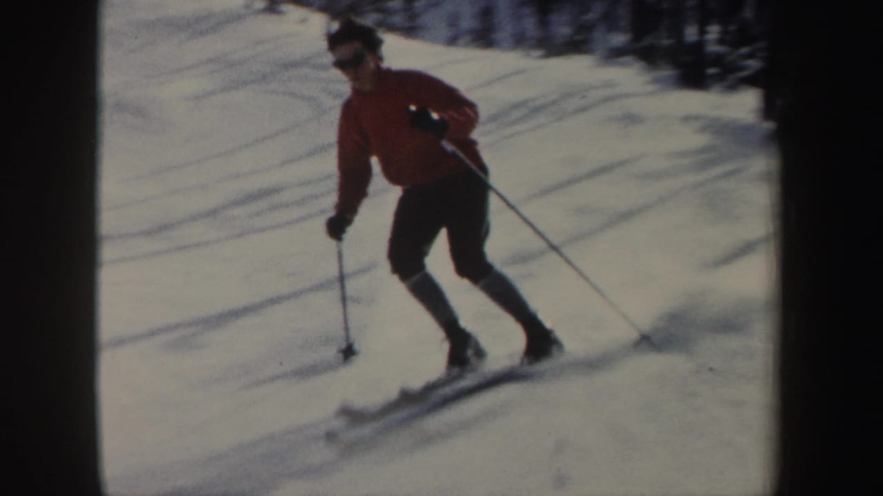 1962 New York 8mm frame showing a skier in a red jacket moving downhill on snow with ski poles near a wooded edge.