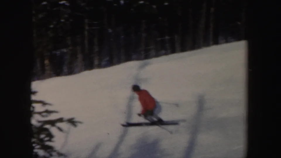 1962 New York 8mm frame showing the skier from behind as he crosses a snow slope near dense winter trees.