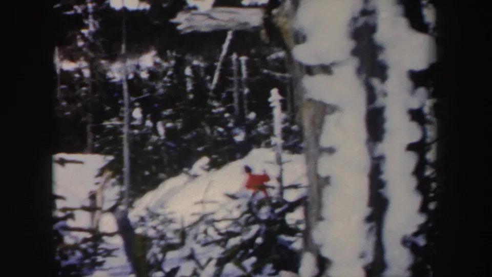 1962 New York home-movie frame with a distant red-jacketed skier moving among snow-covered trees and branches.