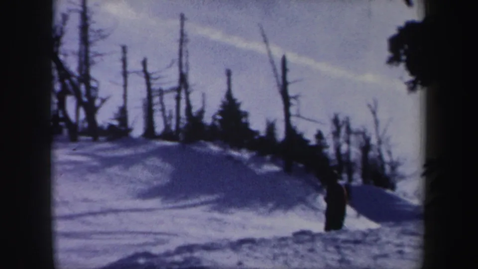 1962 New York 8mm frame showing a wooded snow slope with bare trees and a distant skier.