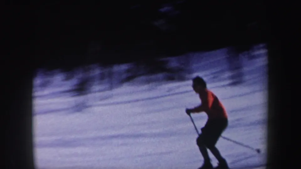 1962 New York 8mm frame of a lone skier in red crossing a snow-covered hillside with ski poles.