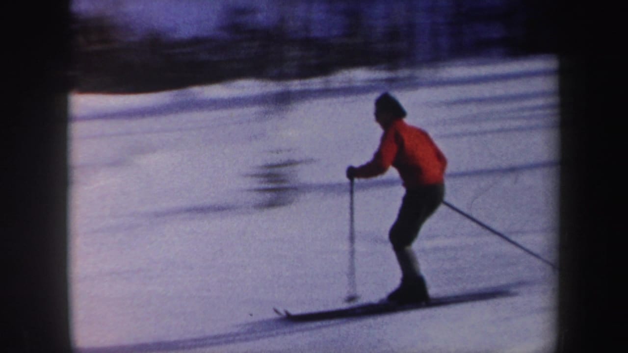 1962 New York 8mm frame showing a skier in a red jacket and dark pants moving across a snowy slope with poles.