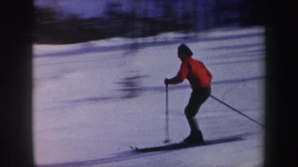 1962 New York 8mm frame showing a skier in a red jacket and dark pants moving across a snowy slope with poles.