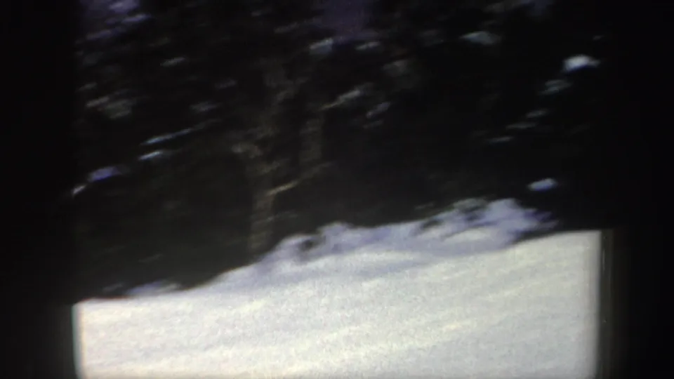 1962 New York 8mm frame showing snowy ground and a dark wooded edge as the skier moves out of the visible frame.
