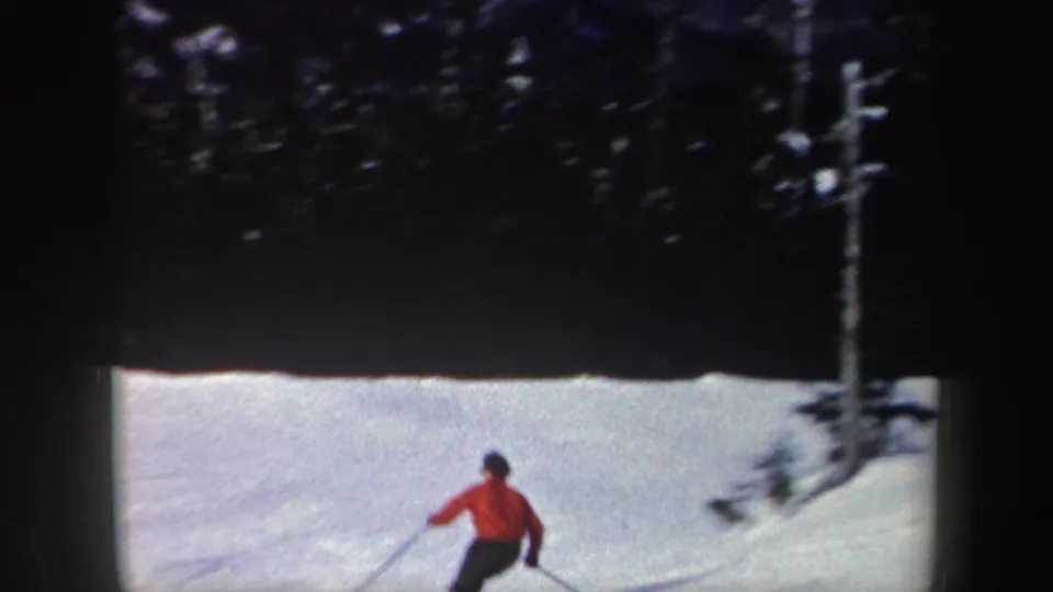 1962 New York 8mm frame showing the red-jacketed skier near the bottom of the frame on a bright snowy slope by trees.