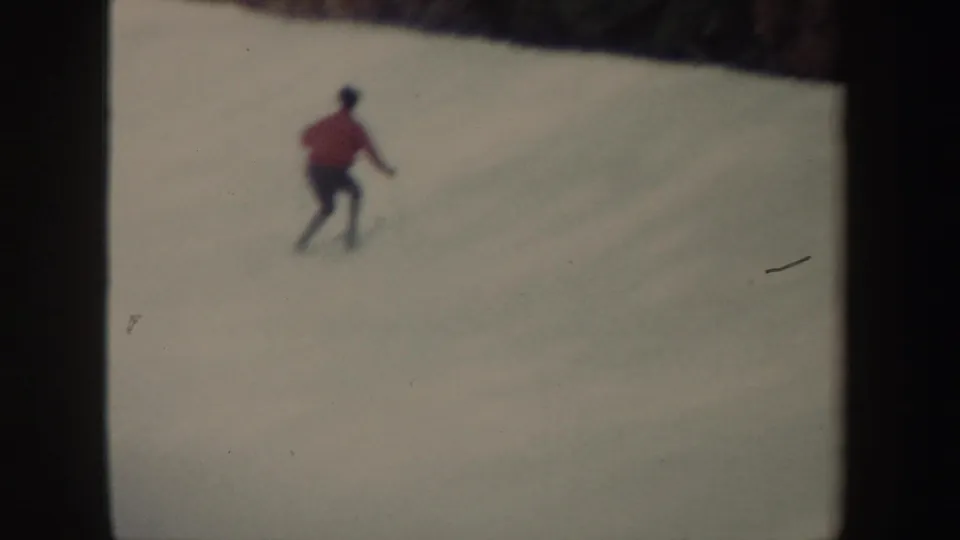 A distant skier in a red jacket and dark pants moves across a snowy New York slope in soft 1962 8mm footage.