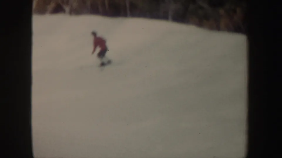 The red-jacketed skier makes a shallow turn across the snow, filmed at a distance in 1962 New York home-movie footage.