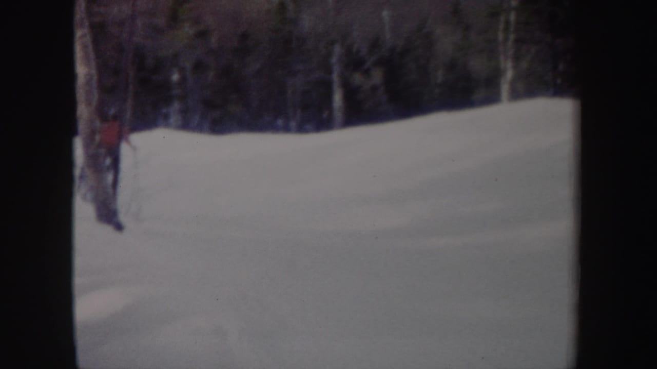 Small skier partly visible at the left edge near trees above a snowy slope.