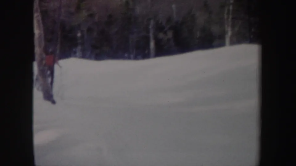 In 1962 New York home-movie footage, a distant skier appears near the left edge of a snowy wooded slope.
