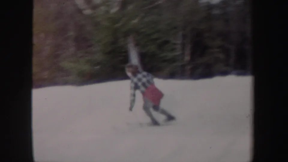 A young woman in a plaid shirt and red skirt skis downhill on a snowy New York slope in 1962 home-movie footage.