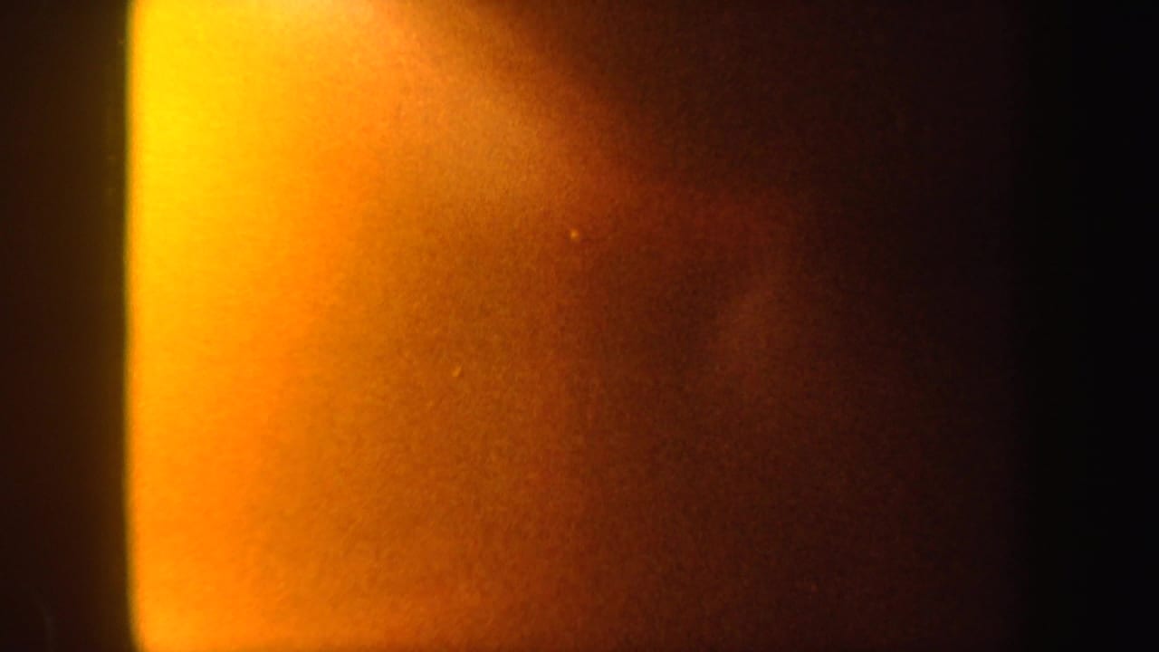 1962 8mm frame showing a bright yellow-orange light leak spreading across an otherwise dark abstract field.