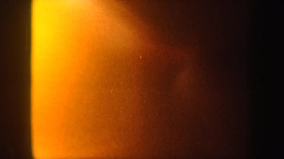 1962 8mm frame showing a bright yellow-orange light leak spreading across an otherwise dark abstract field.
