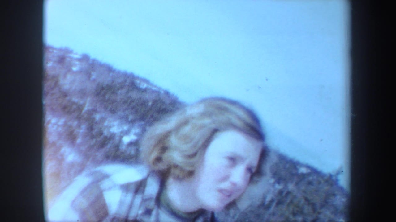 Blonde woman in a plaid coat on a snowy mountain slope.