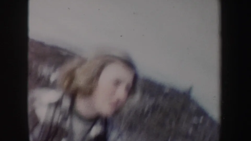 Soft 8mm frame from 1962 New York showing the woman blurred in the foreground against a snowy hillside.