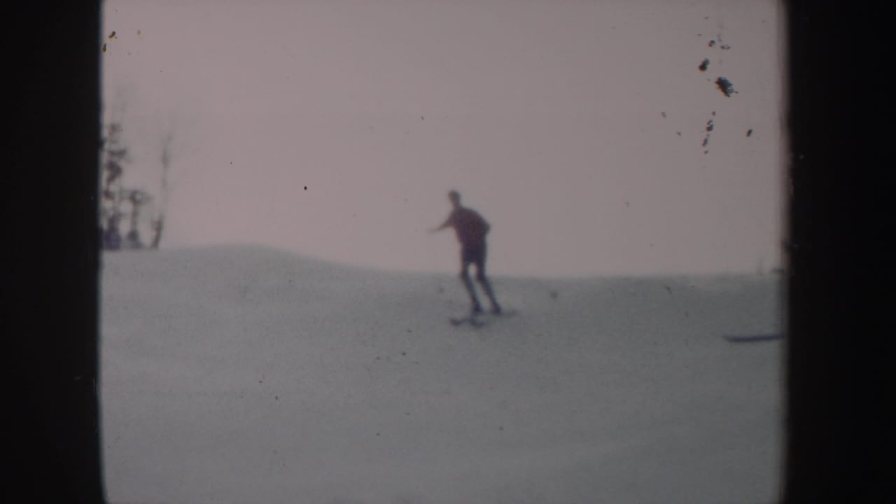 1962 New York 8mm frame showing a distant skier moving across an open snowy slope beneath a pale sky.