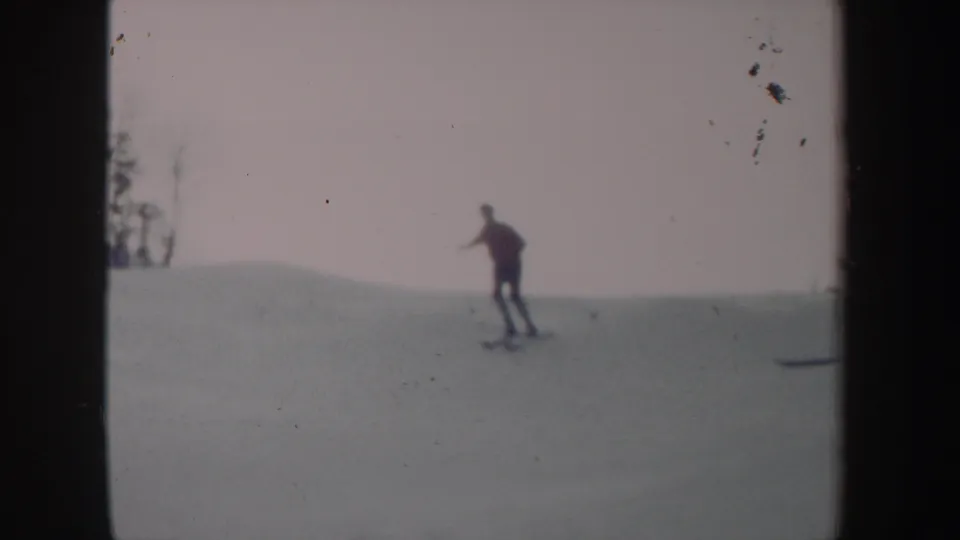 1962 New York 8mm frame showing a distant skier moving across an open snowy slope beneath a pale sky.