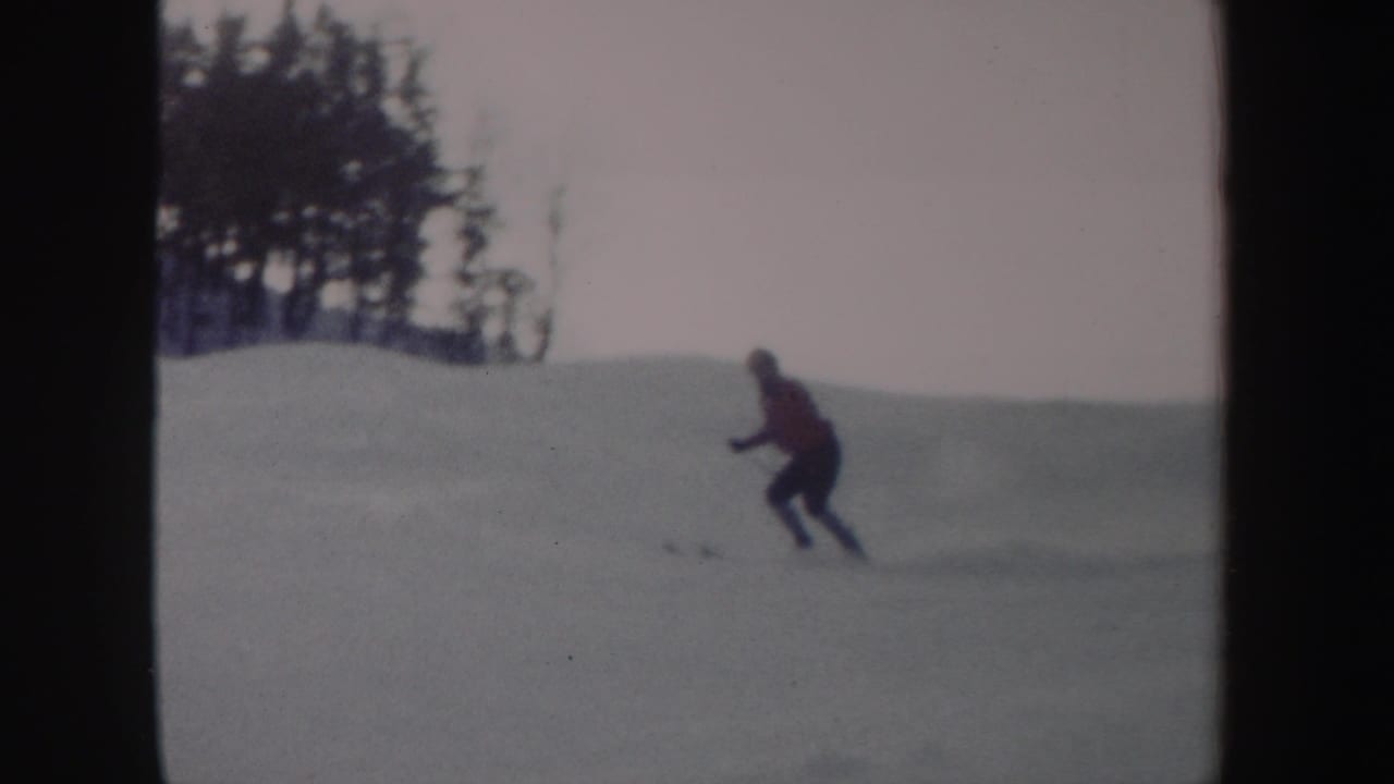 Skier in a red top descends a snowy slope near a tree line.