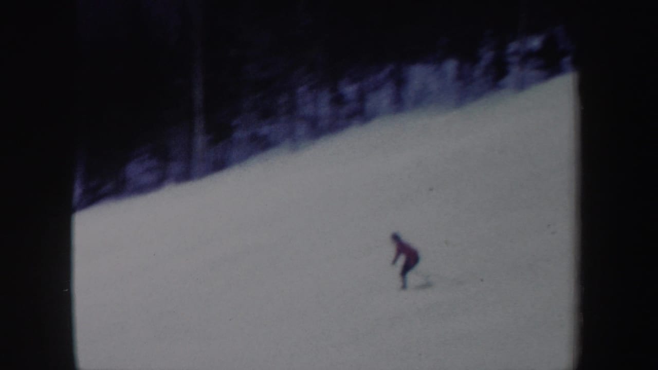 A red-jacketed skier continues down the New York snow slope in a soft, grainy 1962 8mm frame.