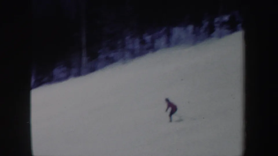A red-jacketed skier continues down the New York snow slope in a soft, grainy 1962 8mm frame.