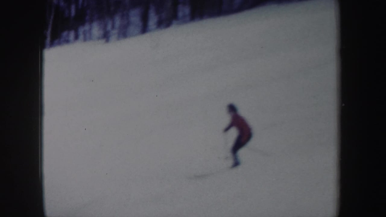 Distant skier in a red jacket descending a snowy hill near dark trees.