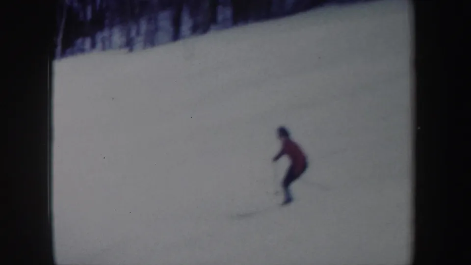 A woman skier in a red jacket moves downhill on a snowy New York slope in 1962 home-movie footage.