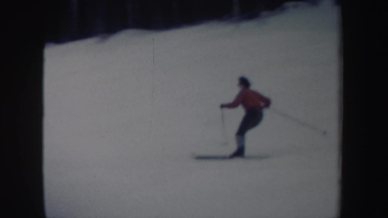 The skier appears in profile with ski poles on the snow-covered hill, framed by dark trees in the distance.