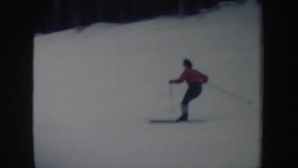 The skier appears in profile with ski poles on the snow-covered hill, framed by dark trees in the distance.
