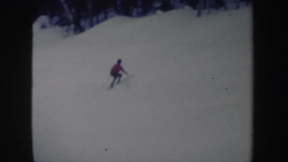1962 New York 8mm frame showing a distant skier in red moving across a snowy hill with trees in the background.