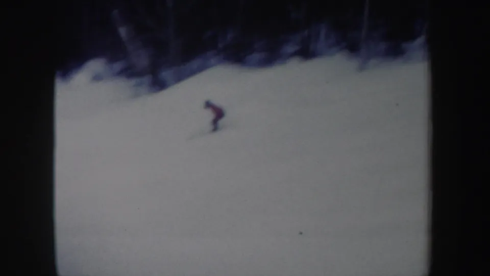 1962 New York 8mm frame showing the red-shirted skier leaning into motion on a snowy slope with trees beyond.