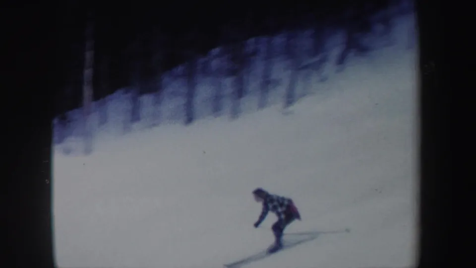 The woman skier leans into a downhill run on a snowy New York slope in this soft 1962 8mm frame.