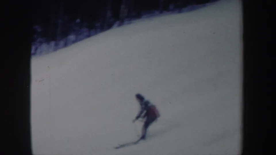 A blurred 8mm frame shows the woman continuing downhill across an open snowy slope with a wooded ridge above.