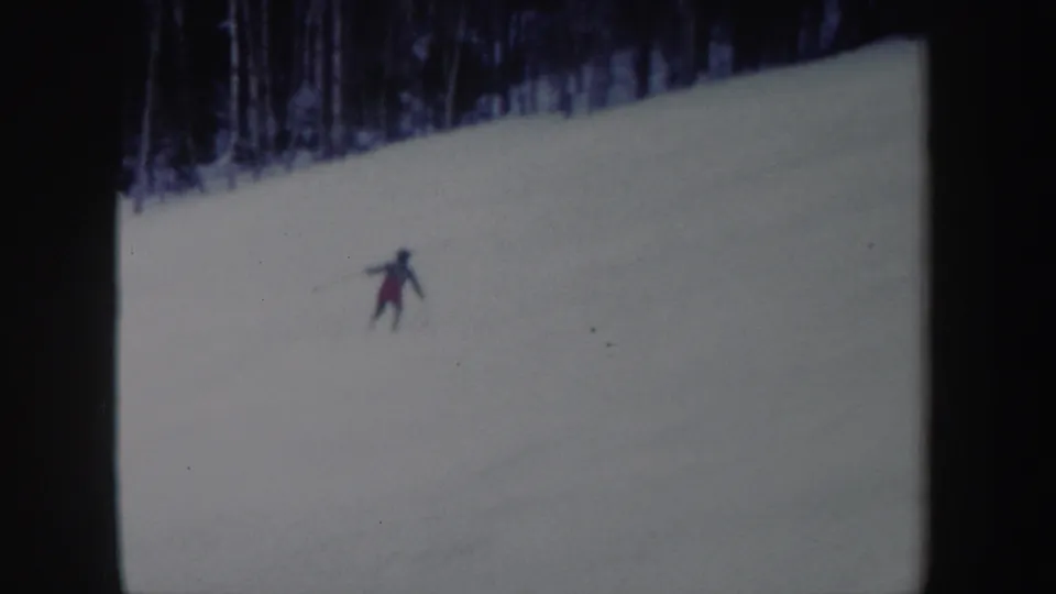 A lone skier in red and dark clothing spreads their arms while crossing the snowy slope in 1962 New York footage.