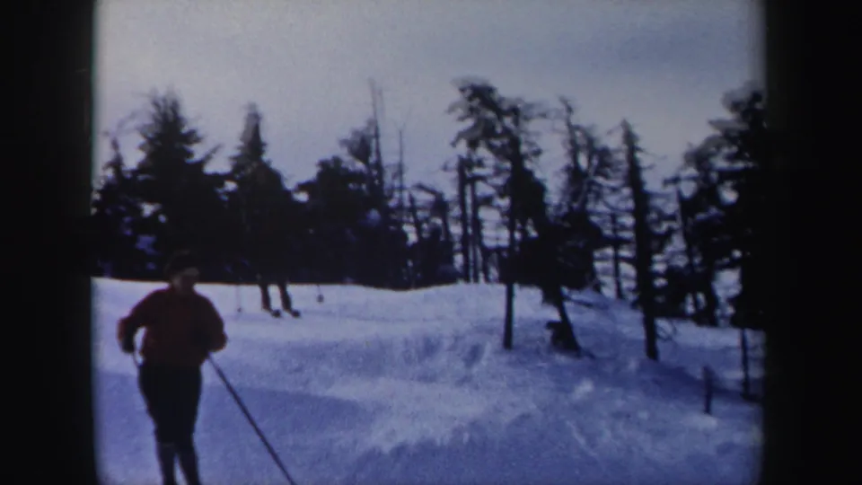 1962 New York 8mm frame showing a skier in a red jacket approaching the camera on a snow-covered wooded slope.